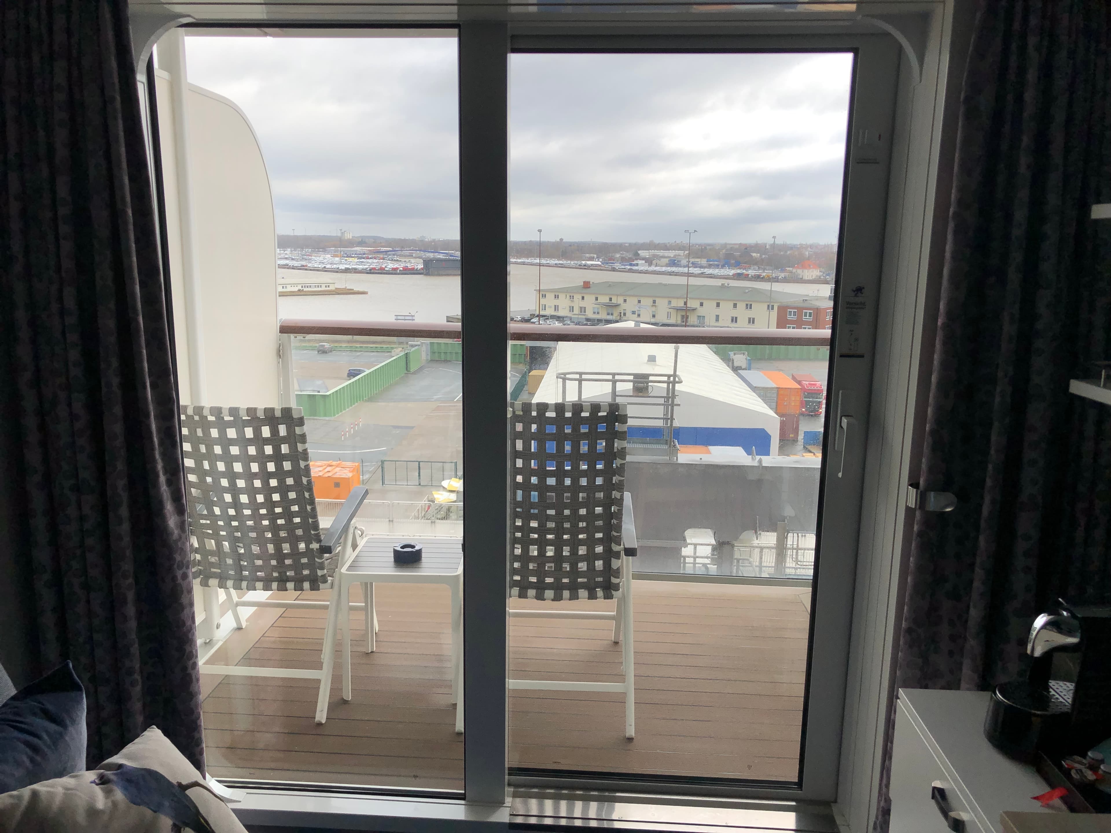 Blick durch die Schiebetür auf Balkon mit zwei Stühlen und Hafenpanorama